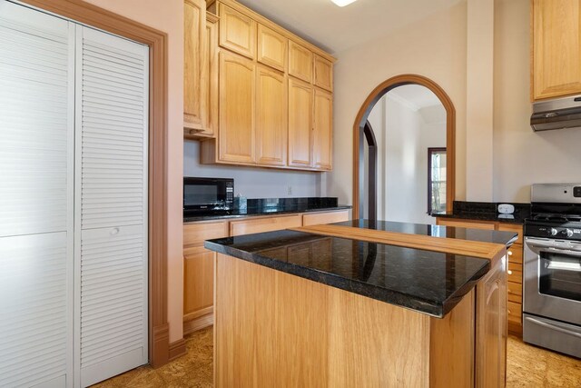 kitchen with dark stone counters, exhaust hood, light brown cabinets, stainless steel range oven, and a kitchen island