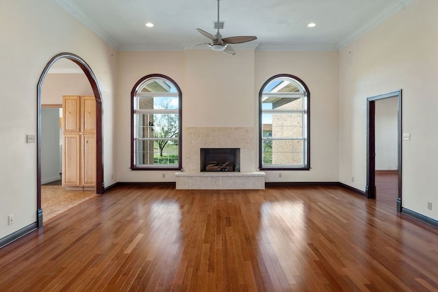 unfurnished living room featuring a tile fireplace, crown molding, hardwood / wood-style floors, and ceiling fan