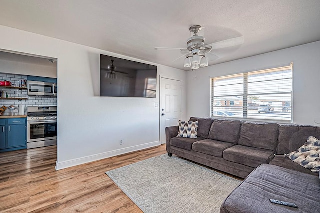 living room with ceiling fan, a textured ceiling, and light wood-type flooring