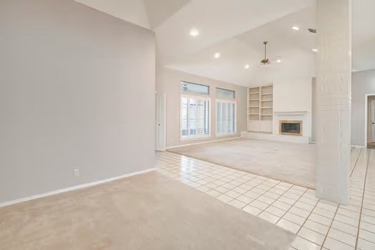 unfurnished living room featuring high vaulted ceiling, light colored carpet, built in features, and ceiling fan