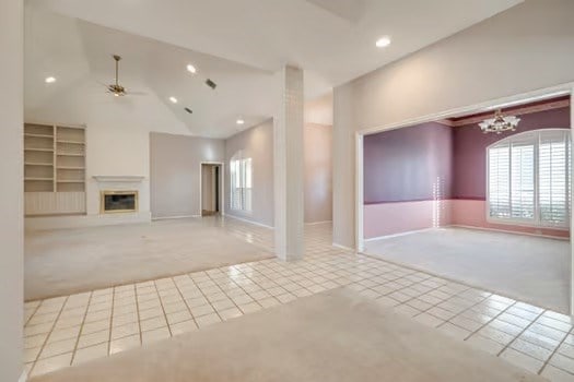 unfurnished living room featuring ceiling fan with notable chandelier, light colored carpet, and high vaulted ceiling