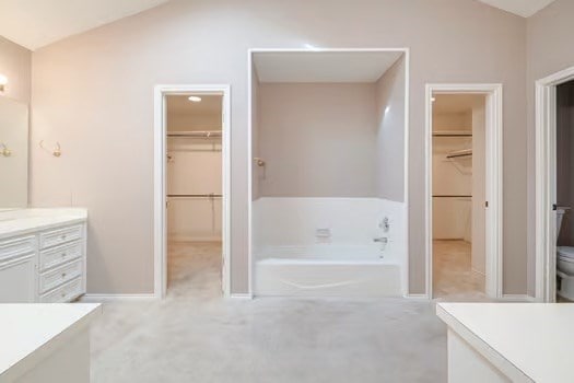 bathroom with a washtub, vanity, lofted ceiling, and toilet