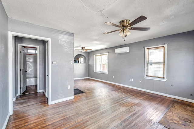 2109 Holloway Ave, Midland, TX 79705 - spare room featuring a ceiling fan, a wall mounted air conditioner, a textured ceiling, wood-type flooring, and baseboards