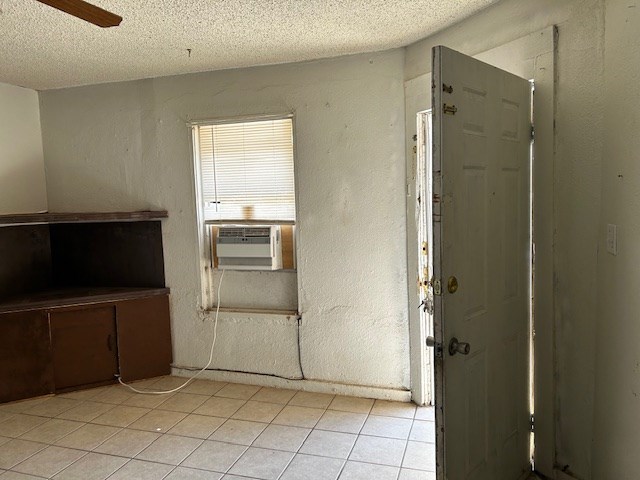 empty room featuring a textured ceiling, cooling unit, and light tile patterned flooring