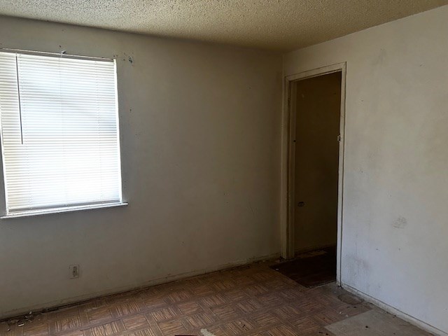 empty room with dark parquet flooring and a textured ceiling