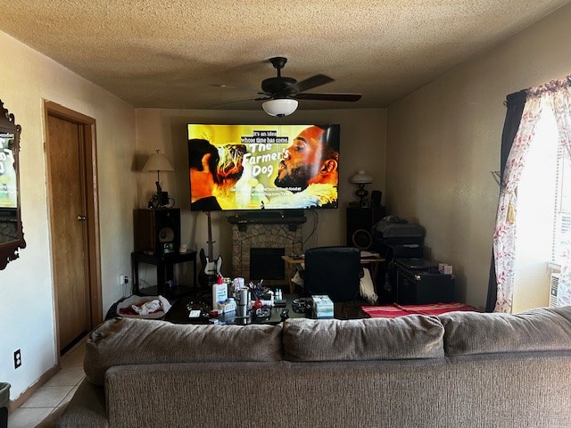 tiled living room featuring ceiling fan, a fireplace, and a textured ceiling