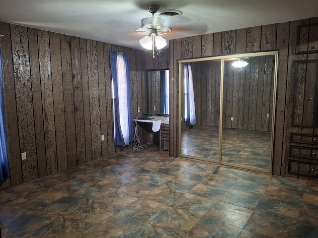 unfurnished bedroom with visible vents, wooden walls, and ceiling fan