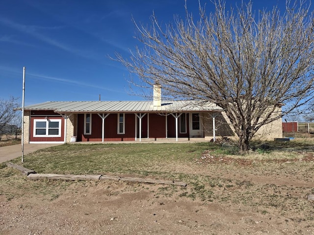 ranch-style home featuring a front lawn, metal roof, a porch, and a chimney