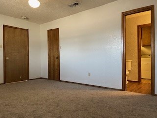 unfurnished bedroom with carpet flooring, a textured ceiling, and ensuite bath