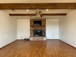 unfurnished living room with a brick fireplace, ceiling fan, hardwood / wood-style flooring, and beamed ceiling