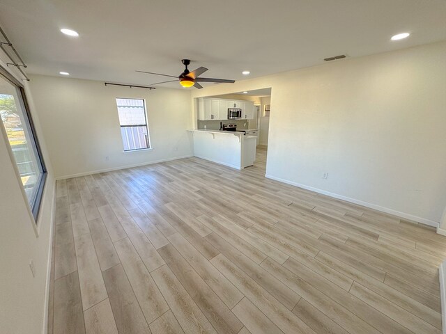 kitchen featuring tasteful backsplash, light hardwood / wood-style flooring, kitchen peninsula, white cabinets, and appliances with stainless steel finishes