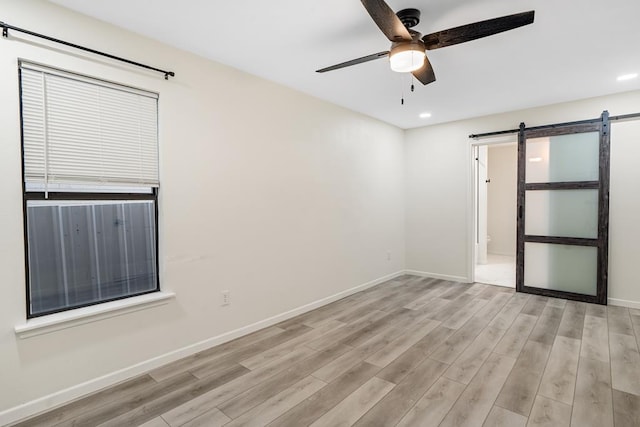 unfurnished room with ceiling fan, a barn door, and light hardwood / wood-style flooring