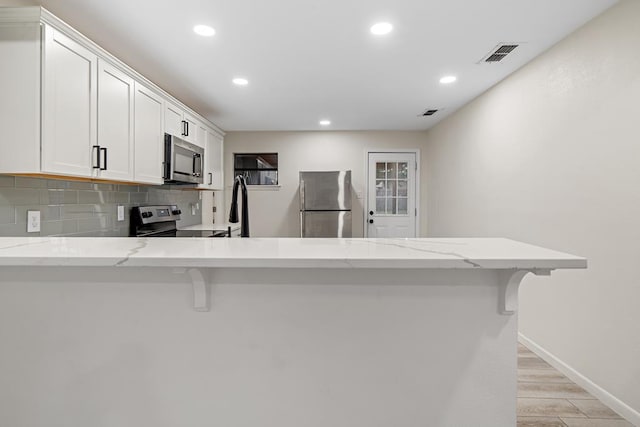 kitchen featuring kitchen peninsula, appliances with stainless steel finishes, white cabinetry, and a kitchen breakfast bar