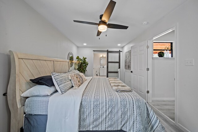 bedroom with ceiling fan, a barn door, and light hardwood / wood-style floors