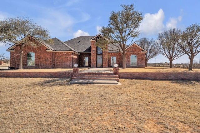 view of front of home with brick siding, a front lawn, and roof with shingles