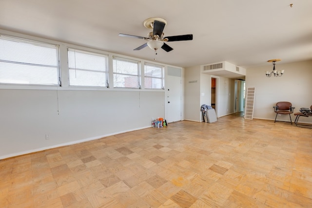 empty room with ceiling fan with notable chandelier, visible vents, and baseboards