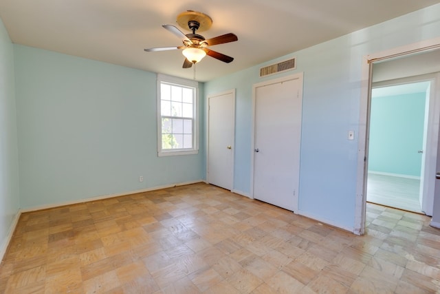 unfurnished bedroom with baseboards, visible vents, a ceiling fan, and multiple closets
