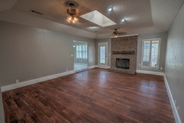 unfurnished living room with a ceiling fan, a textured ceiling, a skylight, wood finished floors, and a fireplace