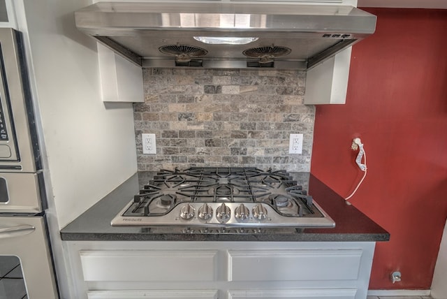 kitchen view of stainless steel gas stovetop, wall chimney exhaust hood, tasteful backsplash, dark countertops, and wall oven
