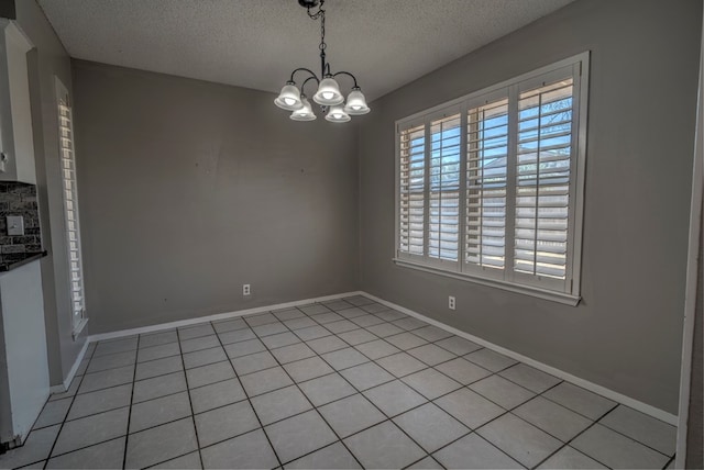 unfurnished dining area with a chandelier, a textured ceiling, light tile patterned flooring, and baseboards