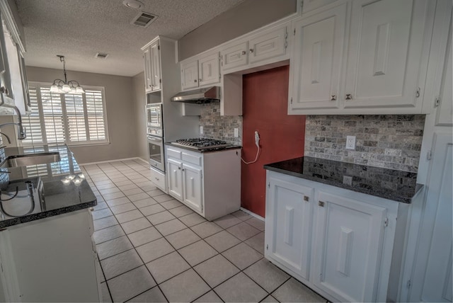 kitchen with a sink, light tile patterned flooring, under cabinet range hood, white cabinetry, and a textured ceiling