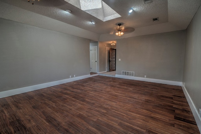 empty room with a skylight, a textured ceiling, wood finished floors, and baseboards
