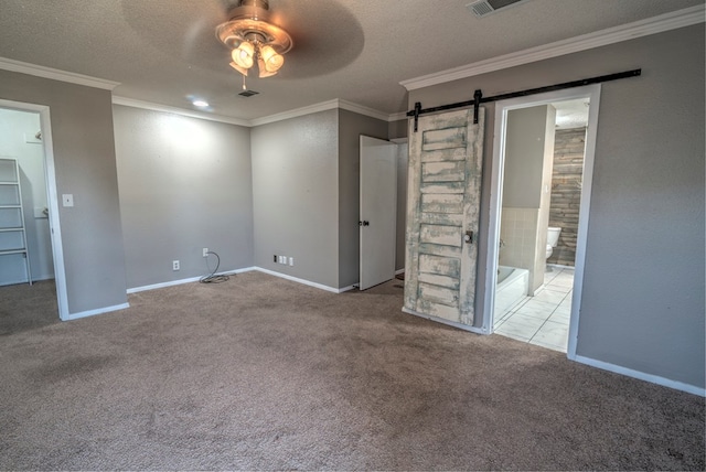 carpeted spare room featuring ceiling fan, a barn door, ornamental molding, baseboards, and a textured ceiling