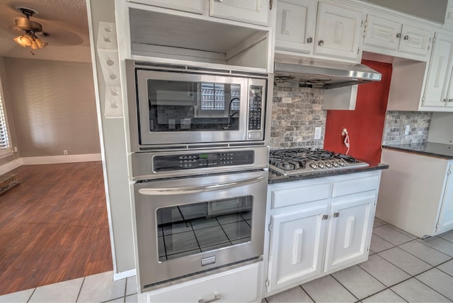 kitchen featuring stainless steel appliances, under cabinet range hood, dark countertops, and tasteful backsplash