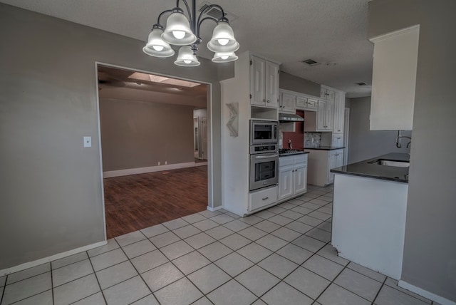 kitchen featuring appliances with stainless steel finishes, a sink, dark countertops, white cabinets, and under cabinet range hood