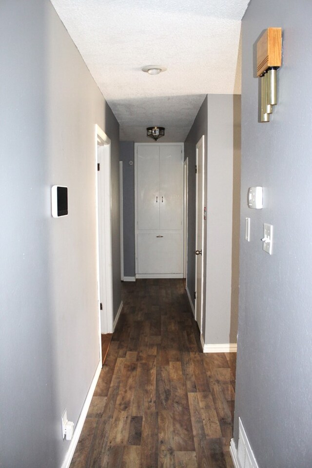 hallway with a textured ceiling and dark hardwood / wood-style flooring