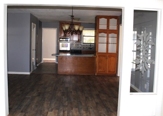 kitchen featuring tasteful backsplash, stainless steel double oven, pendant lighting, a notable chandelier, and dark hardwood / wood-style floors