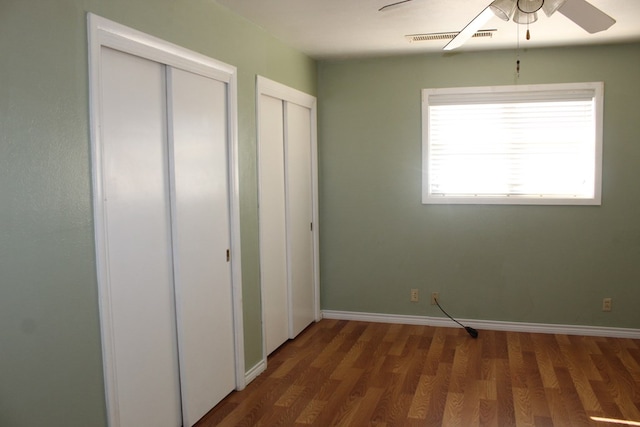 unfurnished bedroom with multiple closets, ceiling fan, and dark hardwood / wood-style flooring