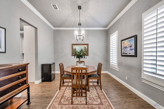 dining space featuring ornamental molding, an inviting chandelier, a textured ceiling, and hardwood / wood-style flooring