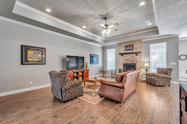 living room with a raised ceiling, wood-type flooring, a fireplace, and crown molding