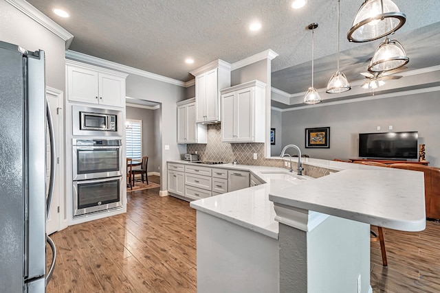 kitchen with pendant lighting, appliances with stainless steel finishes, white cabinets, sink, and kitchen peninsula