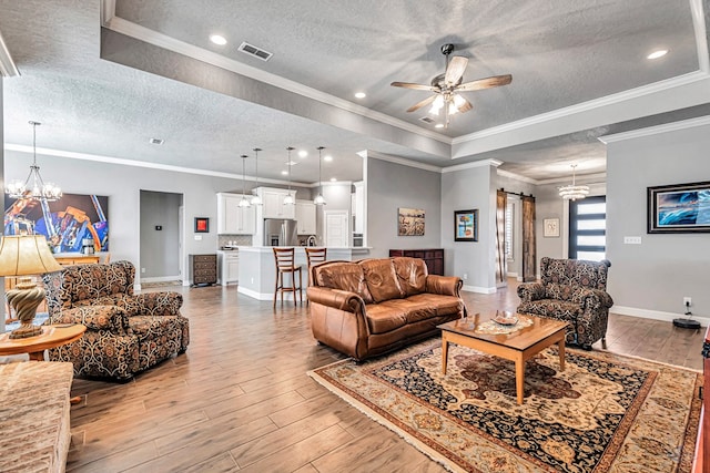 living room with a barn door, a textured ceiling, crown molding, ceiling fan with notable chandelier, and light hardwood / wood-style flooring