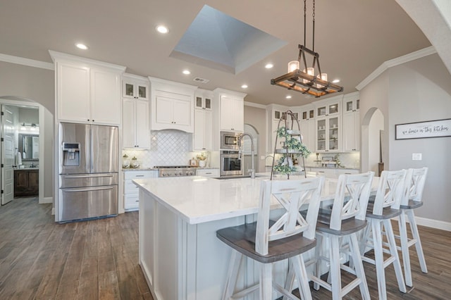 kitchen with arched walkways, a spacious island, glass insert cabinets, appliances with stainless steel finishes, and white cabinetry