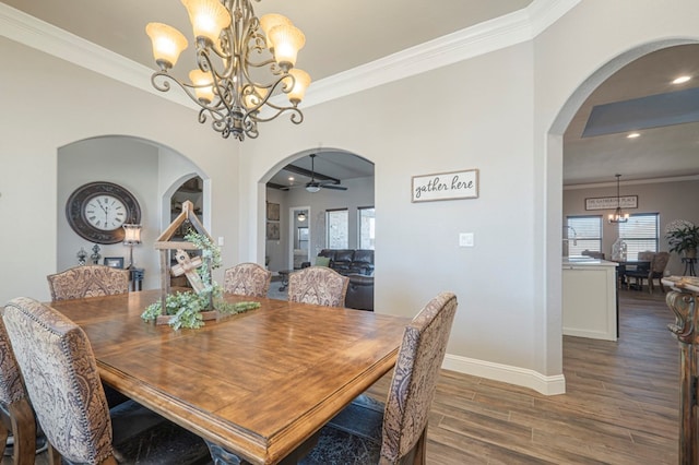 dining area with arched walkways, ceiling fan with notable chandelier, dark wood-type flooring, baseboards, and ornamental molding