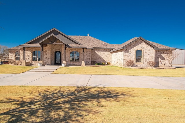 french country style house featuring brick siding, roof with shingles, and a front yard