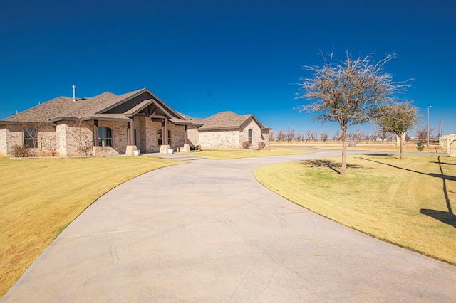 view of front of property featuring curved driveway, a front lawn, and brick siding