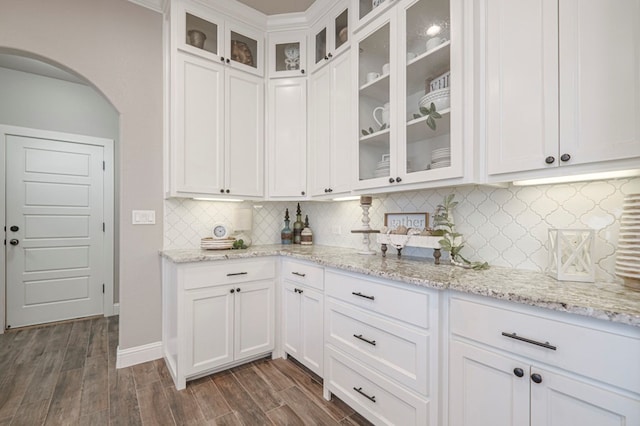 kitchen featuring dark wood finished floors, glass insert cabinets, white cabinets, and arched walkways