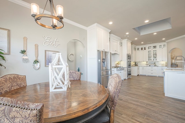 dining area with arched walkways, dark wood-style floors, ornamental molding, an inviting chandelier, and recessed lighting