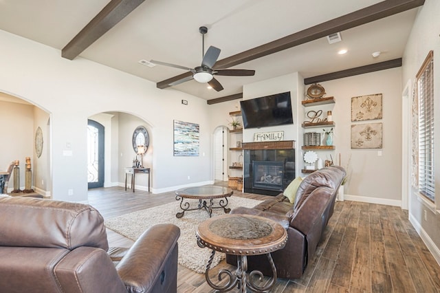 living room with arched walkways, beamed ceiling, dark wood finished floors, and a tile fireplace