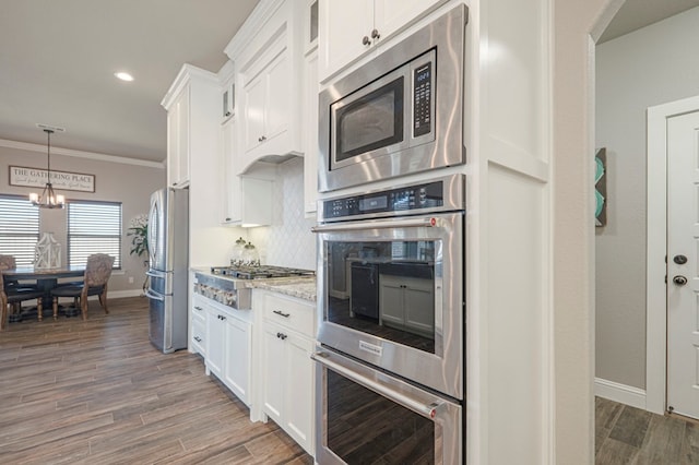 kitchen with appliances with stainless steel finishes, white cabinets, ornamental molding, and light stone counters