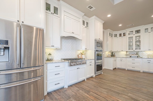 kitchen featuring stainless steel appliances, white cabinets, glass insert cabinets, and light stone counters