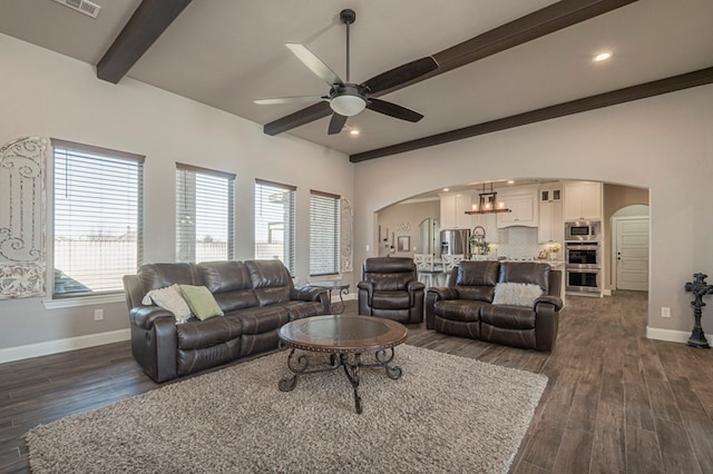 living area featuring dark wood-style floors, arched walkways, beam ceiling, a ceiling fan, and baseboards