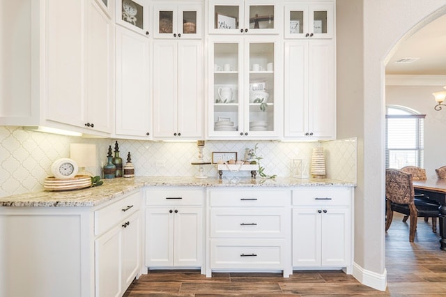 kitchen featuring arched walkways, light stone counters, glass insert cabinets, and white cabinetry