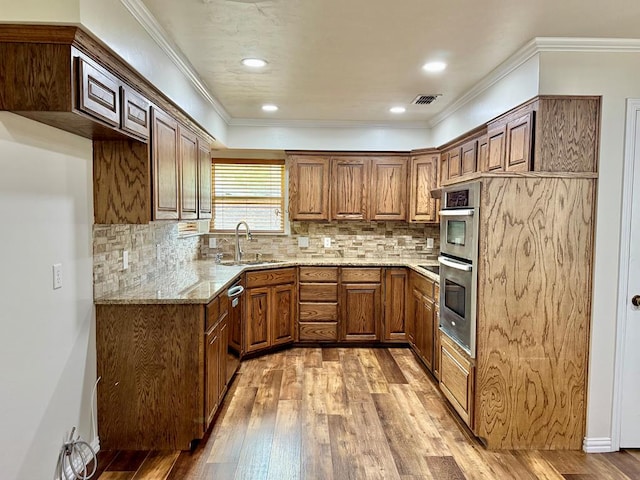 3612 Oakridge Dr, Midland, TX 79707 - kitchen featuring double oven, light wood-type flooring, light stone counters, brown cabinetry, and crown molding