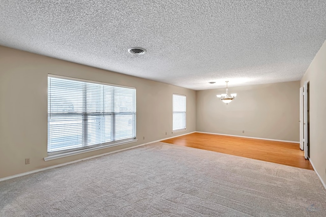 carpeted spare room featuring a chandelier and a textured ceiling