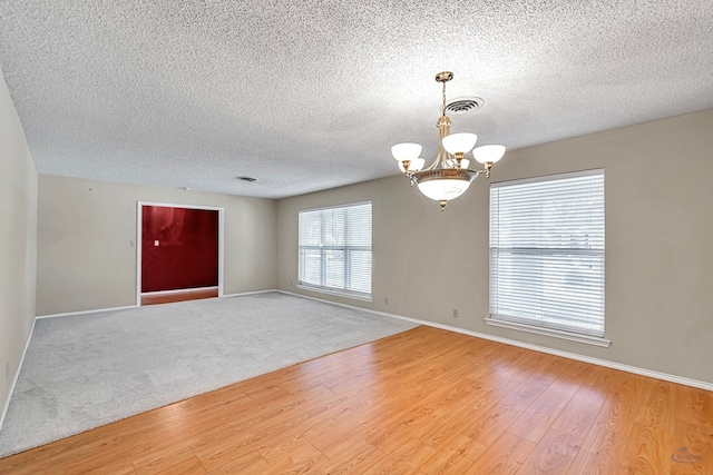 empty room featuring hardwood / wood-style flooring, a chandelier, and a textured ceiling